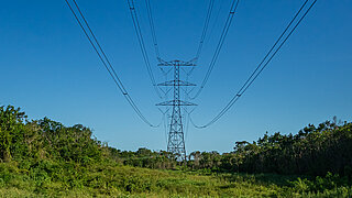 Freistehender Strommast mit mehreren Stromleitungen über einen grünen Landschaft unter blauem Himmel