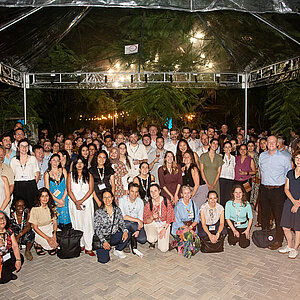 A group photo shows all participants of the IKI network evening. Everyone wears name tags around the neck. Green plants are visible at the edge of the image and beside them are cubes bearing the IKI logo.