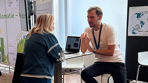 Personen stehen an einem Infostand und unterhalten sich.