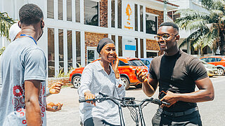 Vier lachende Personen stehen in der Stadt Accra um ein Elektro-Lastenrad und unterhaltne sich.