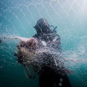 Taucher in Tauchausrüstung hält ein großes Fischernetz unter Wasser