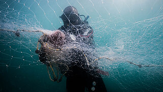 Diver in scuba gear holding a large fishing net underwater