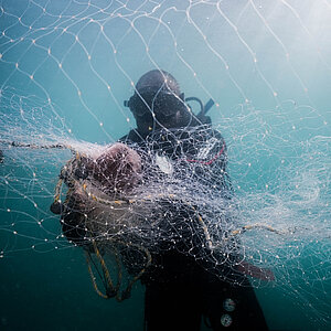 Diver in scuba gear holding a large fishing net underwater