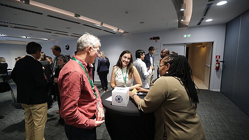 Several people are talking at high tables in a modern, well-lit room