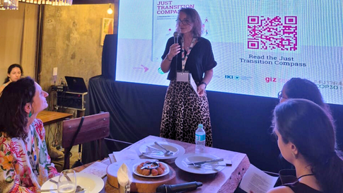 Eine Frau mit Brille und Rock im Leopardenmuster spricht mit Mikrofon vor einer Präsentationswand.