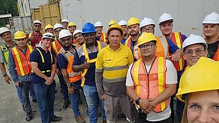 Workers in safety helmets and vests stand for a group photo. They appear friendly.