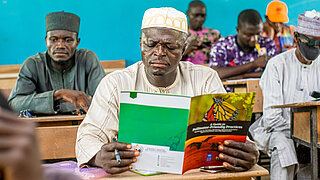 Teilnehmende an einer Schulung in Nigeria lesen in einem Handbuch.