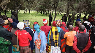 Group of people in colorful clothing standing in a circle in a forest listening to one person