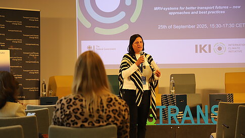 A speaker stands with a microphone on a stage in front of a presentation slide on “Sustainable Mobility.”