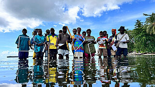 A group of people stands in the shallow ocean waters of Papua New Guinea, taking part in a training session to monitor seagrass meadows and mangrove forests.