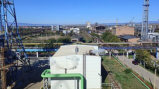 Eine weite Aufnahme eines Industriegebiets mit einem großen Kran und mehreren Anlagen. Das Bild zeigt auch Rohre, die über das Gelände führen.