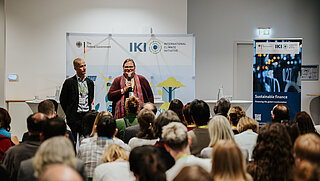 Two speakers on stage in front of a seated audience.
