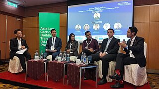 Sechs Personen sitzen auf einer Bühne während einer Podiumsdiskussion zum Thema Energieeffizienz und kohlenstoffarme Gebäude.