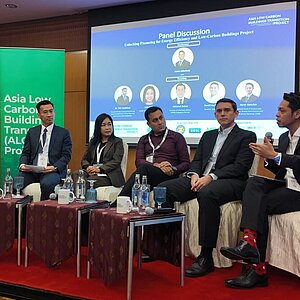 Sechs Personen sitzen auf einer Bühne während einer Podiumsdiskussion zum Thema Energieeffizienz und kohlenstoffarme Gebäude.