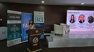 Rednerin am Pult während der NAP Expo 2025, flankiert von Bannern und einer Leinwand mit den Namen und Fotos weiterer angekündigter Vortragender.