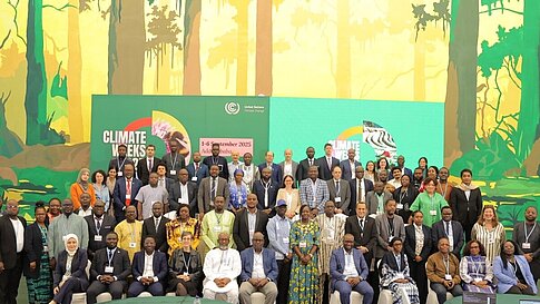 Eine Gruppe von Menschen steht vor einer Wand mit einem großen Klimawand-Plakat und grüner, tropischer Dschungelszene.