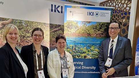 Four persons next to a rollup.