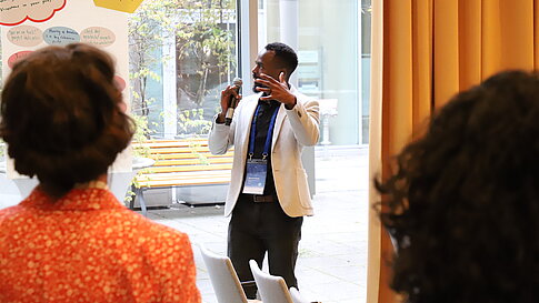 A person speaks to an audience in a conference room while gesturing.