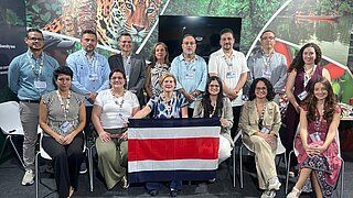 Vierzehn Personen mit einer Flagge Costa Ricas sitzen und stehen bei der Darstellung des CND 3.0 auf der COP30 in Brasilien.