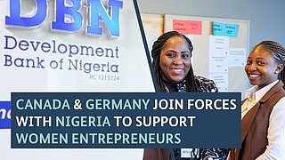 Two women stand next so a sign of the Development Bank of Nigeria