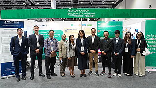 Eine Gruppe von elf Fachleuten steht gemeinsam vor einem Ausstellungsstand des Projekts „Asia Low Carbon Buildings Transition Project“ auf einer Konferenz.