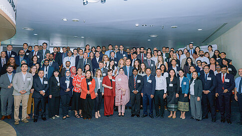 Große Gruppe von Fachleuten posiert für ein Gruppenfoto in einem Konferenzraum.