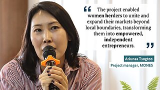 A woman speaks into a microphone, explaining a project that helps women herders expand their markets and become independent entrepreneurs.