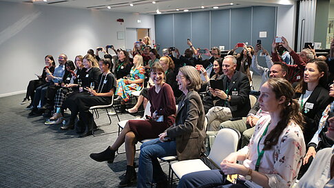 Group of people sitting in a room holding up smartphones