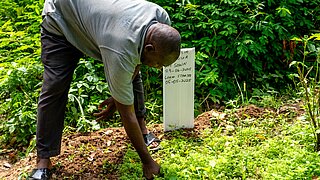 Ein nigerianischer Landwirt fährt mit einer Hadn über den Boden und präsentiert lokale Pflanzenarten auf einer Demonstrationsfläche für Heilpflanzen.
