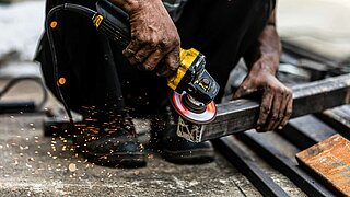 Ein Mann hockt am Boden und bearbeitet mit einem Werkzeug ein Metallstück.