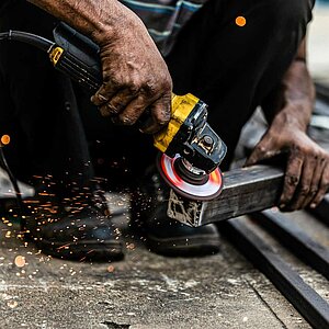 Ein Mann hockt am Boden und bearbeitet mit einem Werkzeug ein Metallstück.