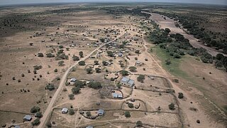 Luftaufnahme einer weitläufigen, trockenen Landschaft mit verstreuten Gebäuden und vereinzeltem Baumbestand