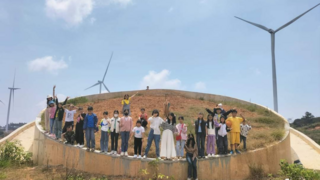 Eine Gruppe von JUgendlichen steht in Vietnam im Kreis unter blauem Himmel und einem Windrad.
