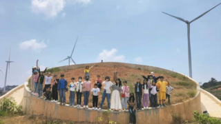 Eine Gruppe von JUgendlichen steht in Vietnam im Kreis unter blauem Himmel und einem Windrad.