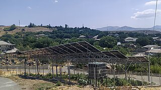 Freistehende Agri-Photovoltaikanlage mit Solarmodulen auf Metallgestell über landwirtschaftlicher Fläche in ländlicher Umgebung Armeniens mit Hügeln und Häusern im Hintergrund