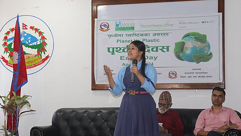 Frau spricht während einer Earth-Day-Feier mit Banner im Hintergrund.