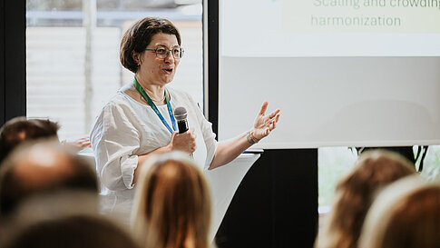 Woman speaking to the audience next to a presentation slide.