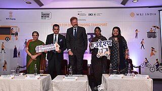drei Frauen und zwei Männer stehen auf einer Konferenz auf der Bühne und halten ein Schild mit dem Hashtag WomenInTransport in den Händen