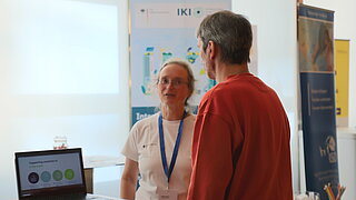 Personen stehen an einem Infostand und unterhalten sich.