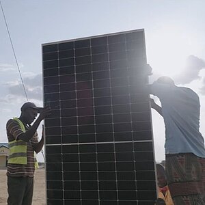 Zwei Personen installieren ein großes Solarpanel im Freien bei hellem Tageslicht