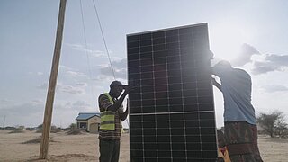 Zwei Personen installieren ein großes Solarpanel im Freien bei hellem Tageslicht