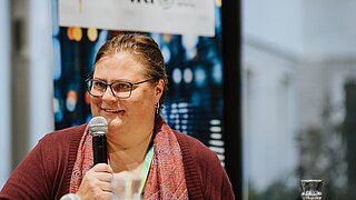 Andrea Kämpf, Leiterin der Geschäftsstelle des Unabhängigen Beschwerdemechanismus der IKI, spricht auf einer Veranstaltung auf der Bühne in ein Mikrofon.