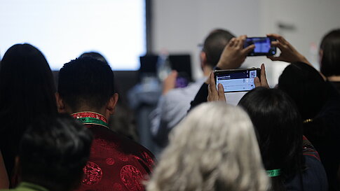 Rear view of several people in a room, some holding up smartphones to take photos or videos.