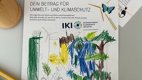 A sheet of paper with an environmental and climate protection theme, colored by a child. The paper also features stickers of various eco-friendly symbols.