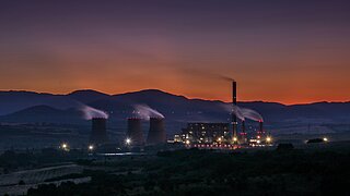 Eine große Industrieanlage liegt in einer weiten, menschenleeren Landschaft, während die Sonne bereits fast untergegangen ist.
