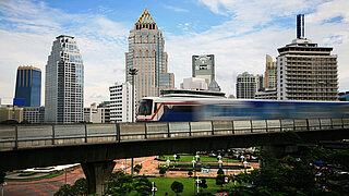 A train crosses a bridge. Skyscrapers can be seen in the distance. 