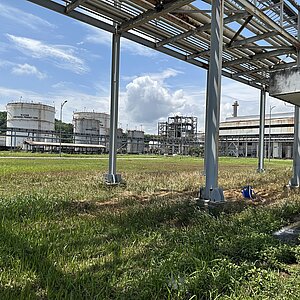 Industrieanlage mit großen zylindrischen Tanks und Rohrleitungen auf einer Wiese unter blauem Himmel mit Wolken