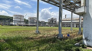 Industrieanlage mit großen zylindrischen Tanks und Rohrleitungen auf einer Wiese unter blauem Himmel mit Wolken