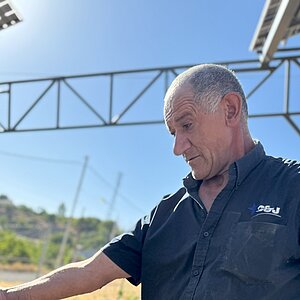 Ein Mann in einem kurzärmligen Hemd steht unter einer Solaranlage und blickt nach unten.