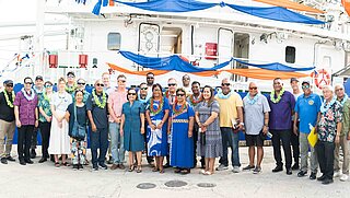 Eine Gruppe steht vor einem Schiff. 